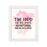 Bible wall art featuring The Lord Is My Rock, My Fortress, and My Deliverer in black handwritten-style lettering on a soft pink watercolor background. hung on the wall in a white frame