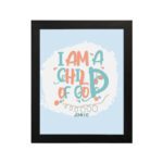 I Am a Child of God Christian Wall Art in bright orange and turquoise with a pastel blue background, perfect for home decor. hung on the wall in a black frame