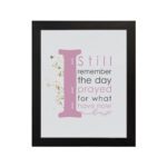 Christian wall art featuring the phrase 'I Still Remember The Days I Prayed For What I Have Now' with pink and gray text and gold flowers. hung on the wall in a black frame