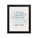 Christian wall art featuring the phrase I Still Remember The Days I Prayed For What I Have Now with floral designs in light blue. hung on the wall in a black frame