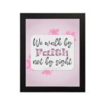 Christian wall art displaying We Walk By Faith Not By Sight with floral elements on a pale pink background. hung on the wall in a black frame