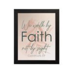 Christian wall art displaying the quote We Walk By Faith Not By Sight in elegant fonts on a soft beige-pink background. hung on the wall in a black frame