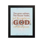 The Grass Withers Christian wall art with the verse Isaiah 40:8 in a modern font, featuring floral illustrations and a light blue background. hung the wall in a black frame