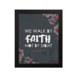 Christian wall art with 2 Corinthians 5:7 Bible verse on a light black background with a pink flower in the corner and white font and black framed displayed on the wall