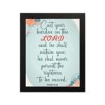 Cast Your Burden on the Lord Psalm 55:22 Christian wall art with teal and coral text on a mint green background with floral accents. hung on the wall in a black frame