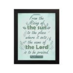 Wall art displaying Psalm 113:3 with elegant cursive font and leafy motifs on a mint green background. hung on the wall in a black frame