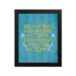 Christian wall art with Proverbs 31:25 verse in bold yellow text on a dark blue background with floral accents hung on the wall in a black frame