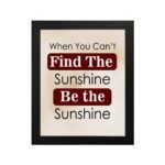 Infidu motivational wall art featuring the quote When You Can't Find the Sunshine Be the Sunshine on a white background with red text and a black frame hung on the wall. perfect for office decor.