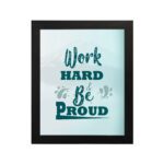 Work Hard Be Proud office wall art featuring green text with decorative elements on a white background, framed in black hung on the wall. Perfect for home offices.