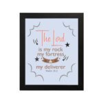 The Lord Is My Rock My Fortress And My Deliverer Psalm 18:2 Bible Wall Art with red, brown, and black text on a light blue background. hung on the wall in a black frame