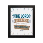 Bible wall art featuring The Lord Is My Rock, My Fortress, and My Deliverer in blue and tan text on a white background with decorative lines. hung on the wall in a black frame