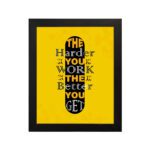 Infidu The Harder You Work The Better You Get wall art with a yellow background and dark yellow and white text with black shadow and black frame hung on the wall. Inspiring decor for home offices and workspaces.