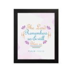 Wall art featuring The Lord Remembers Us And Will Bless Us Psalm 115:12 in pastel colors with leaf accents on a soft background. hung on the wall in a black frame