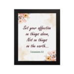 Infidu Bible wall art with Colossians 3:2 in dark brown text, surrounded by peach and beige flowers on a cream background. hung on the wall in a black frame