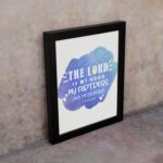 Bible wall art with The Lord Is My Rock, My Fortress, and My Deliverer in white stencil-style text on a blue watercolor background. displayed on the wall in a black frame