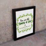 You Are The Temple Of God, His Spirit Dwells In You 1 Corinthians 3:16 Bible Verse Wall Art with green leaf wreath design. displayed on the wall in a black frame