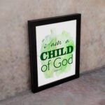 I Am A Child Of God wall art in elegant fonts with a green and black color scheme on a soft green watercolor background. displayed on the wall in a black frame