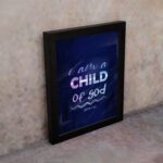 Infidu I Am A Child Of God wall art featuring soft glowing text in pink and blue on a dark blue background. displayed on the wall in a black frame