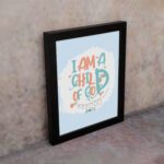 I Am a Child of God Christian Wall Art in bright orange and turquoise with a pastel blue background, perfect for home decor. displayed on the wall in a black frame