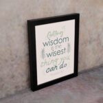 Infidu wall art with Proverbs 4:7 text surrounded by green leaves on a beige background. Elegant and minimal design. displayed on the wall in a black frame