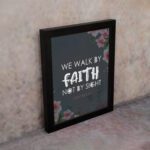 Christian wall art with 2 Corinthians 5:7 Bible verse on a light black background with a pink flower in the corner and white font and black framed on the wall