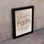 Christian wall art displaying the quote We Walk By Faith Not By Sight in elegant fonts on a soft beige-pink background. displayed on the wall in a black frame