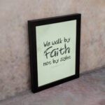 We Walk By Faith Not By Sight Bible Verse Wall Art on a mint green background. displayed on the wall in a black frame