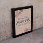 We Walk By Faith Not By Sight Christian Wall Art with pink roses and gray leaves on a soft pink background displayed on the wall in a black frame.