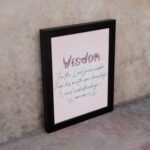 Christian wall art with the quote from Proverbs 2:6, featuring the word "Wisdom" in script on a soft pink background. displayed on the wall in a black frame