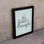 His Grace Is Enough Bible wall art with a mint background and teal script design, surrounded by decorative elements. displayed on the wall in a black frame