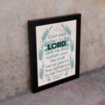 Cast Your Burden on the Lord Psalm 55:22 Christian Wall Art with palm leaf accents and turquoise text on a beige background. displayed on the wall in a black frame