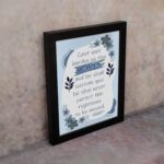 Christian wall art featuring Psalm 55:22 with navy blue text on a light blue and white background, decorated with blue flowers. displayed on the wall in a black frame