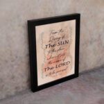 Bible wall art featuring Psalm 113:3 with floral elements and stylish text on a peach background. displayed on the wall in a black frame