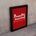 Infidu Dream Big Work Hard Make It Happen wall art with a red background white and yellow text and a black frame on the wall. Inspiring decor for home offices and workspaces.