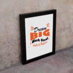 Infidu Dream Big Work Hard Make It Happen wall art with a gray background black and orange text and a black frame on the wall. Inspiring decor for home offices and workspaces.