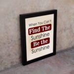 Infidu motivational wall art featuring the quote When You Can't Find the Sunshine Be the Sunshine on a white background with red text and a black frame on the wall. perfect for office decor.