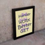 Infidu The Harder You Work The Better You Get wall art with a light sandal background and dark blue and violet text and black frame on the wall. Inspiring decor for home offices and workspaces.