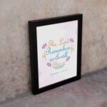 Wall art featuring The Lord Remembers Us And Will Bless Us Psalm 115:12 in pastel colors with leaf accents on a soft background. displayed on the wall in a black frame