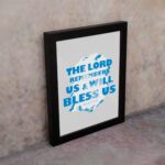 Wall art featuring the text The Lord Remembers Us And Will Bless Us in bold blue on a soft gray background. displayed on the wall in a black frame