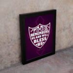 The Lord Remembers Us and Will Bless Us Psalm 115:12 Bible Verse Wall Art in bold white text on a deep purple background. displayed on the wall in a black frame