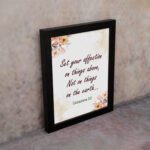 Infidu Bible wall art with Colossians 3:2 in dark brown text, surrounded by peach and beige flowers on a cream background. displayed on the wall in a black frame