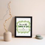 You Are The Temple Of God, His Spirit Dwells In You 1 Corinthians 3:16 Bible Verse Wall Art with green leaf wreath design. displayed on the wall in a black frame