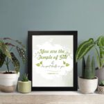 Christian wall art featuring 'You Are The Temple of God His Spirit Dwells in You' from 1 Corinthians 3:16 with green and gray design. displayed on the table in a black frame