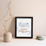 Christian wall art with You are the Temple of God in blue calligraphy and decorative blue dot patterns on a white background. displayed on the wall in a black frame