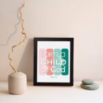 Infidu I Am A Child Of God John 1:12 Christian Wall Art with modern pink and green gradient design on a playful background. displayed on the wall in a black frame