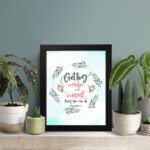 Proverbs 4:7 Bible verse wall art with green leaf wreath and red flowers, perfect for Christian home decor. displayed on the table in a black frame