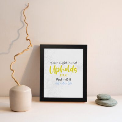 Christian wall art featuring the phrase Your Right Hand Upholds Me in playful fonts with a yellow cursive style and decorative waves. displayed on the wall in a black frame