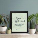 Your Right Hand Upholds Me Psalm 63:8 Christian wall art with dark gray text and light green floral elements on a pale green displayed on the table in a black frame background.