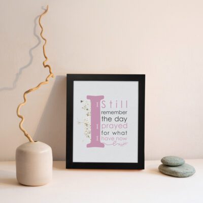 Christian wall art featuring the phrase 'I Still Remember The Days I Prayed For What I Have Now' with pink and gray text and gold flowers. displayed on the wall in a black frame