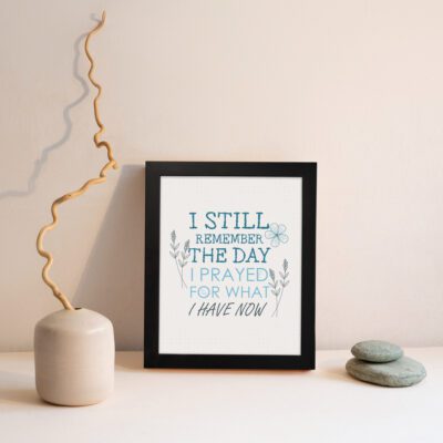 Christian wall art featuring the phrase I Still Remember The Days I Prayed For What I Have Now with floral designs in light blue. displayed on the wall in a black frame